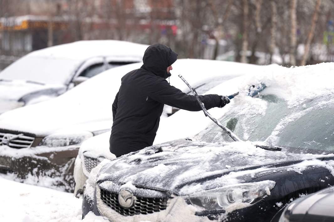 Мужчина расчищает автомобиль после снегопада