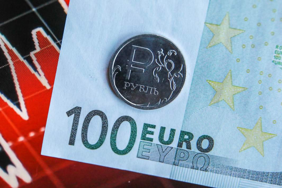 Купюра номиналом сто евро и монета достоинством один российский рубль на фоне биржевого графика