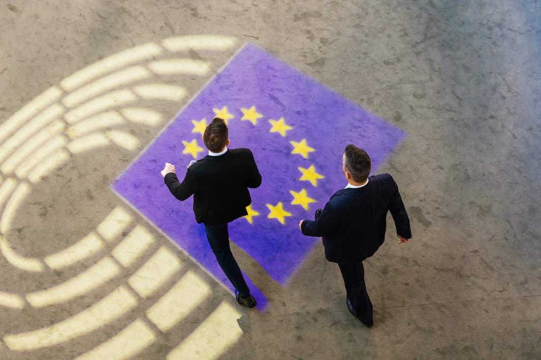 Двое мужчин проходят мимо проекции логотипа Европейского парламента