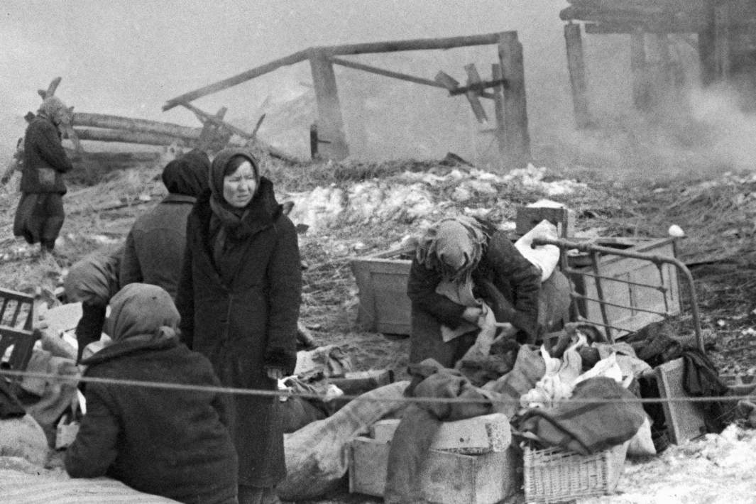 Мирные жители возвращаются к своим домам, чтобы собрать уцелевшие остатки своего имущества на месте сгоревшей деревни