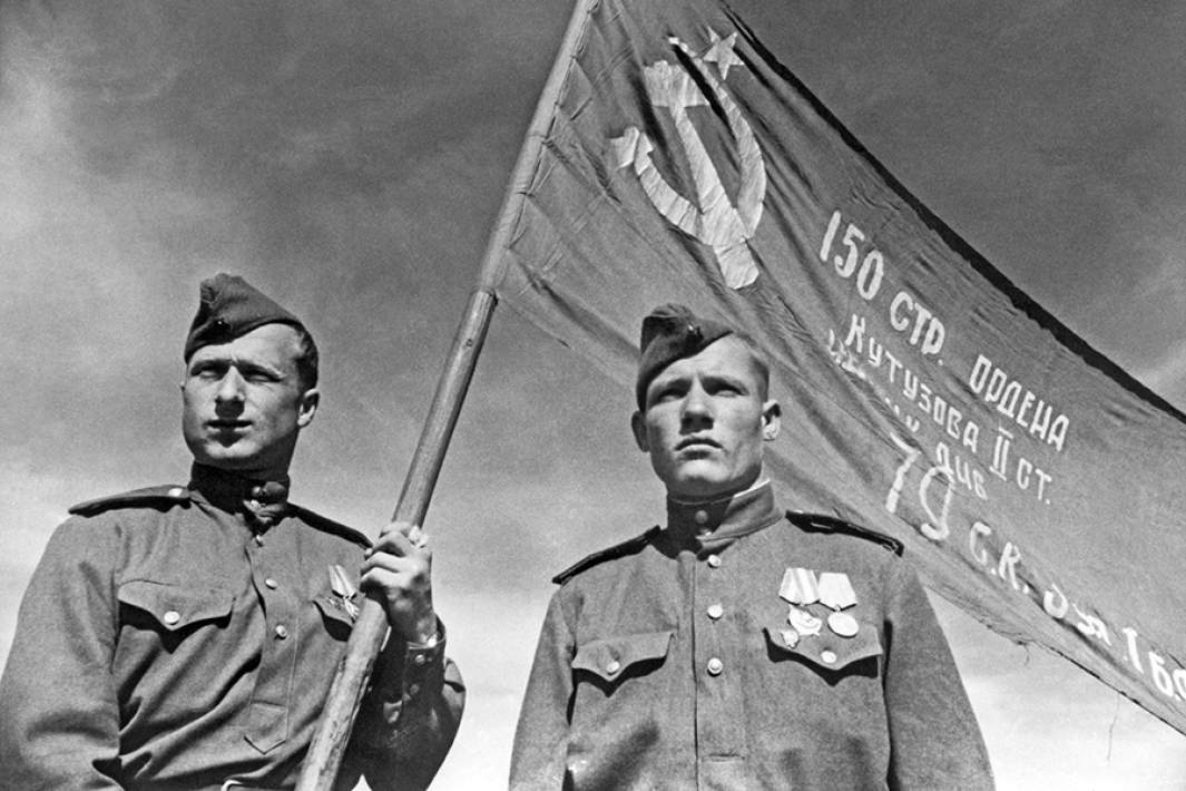 Советские фронтовые разведчики младший сержант Мелитон Варламович Кантария и сержант Михаил Алексеевич Егоров (слева направо) со штурмовым флагом 150-й Идрицкой ордена Кутузова II степени стрелковой дивизии, который был водружен ими на крыше здания Рейхстага. 2 мая 1945 года