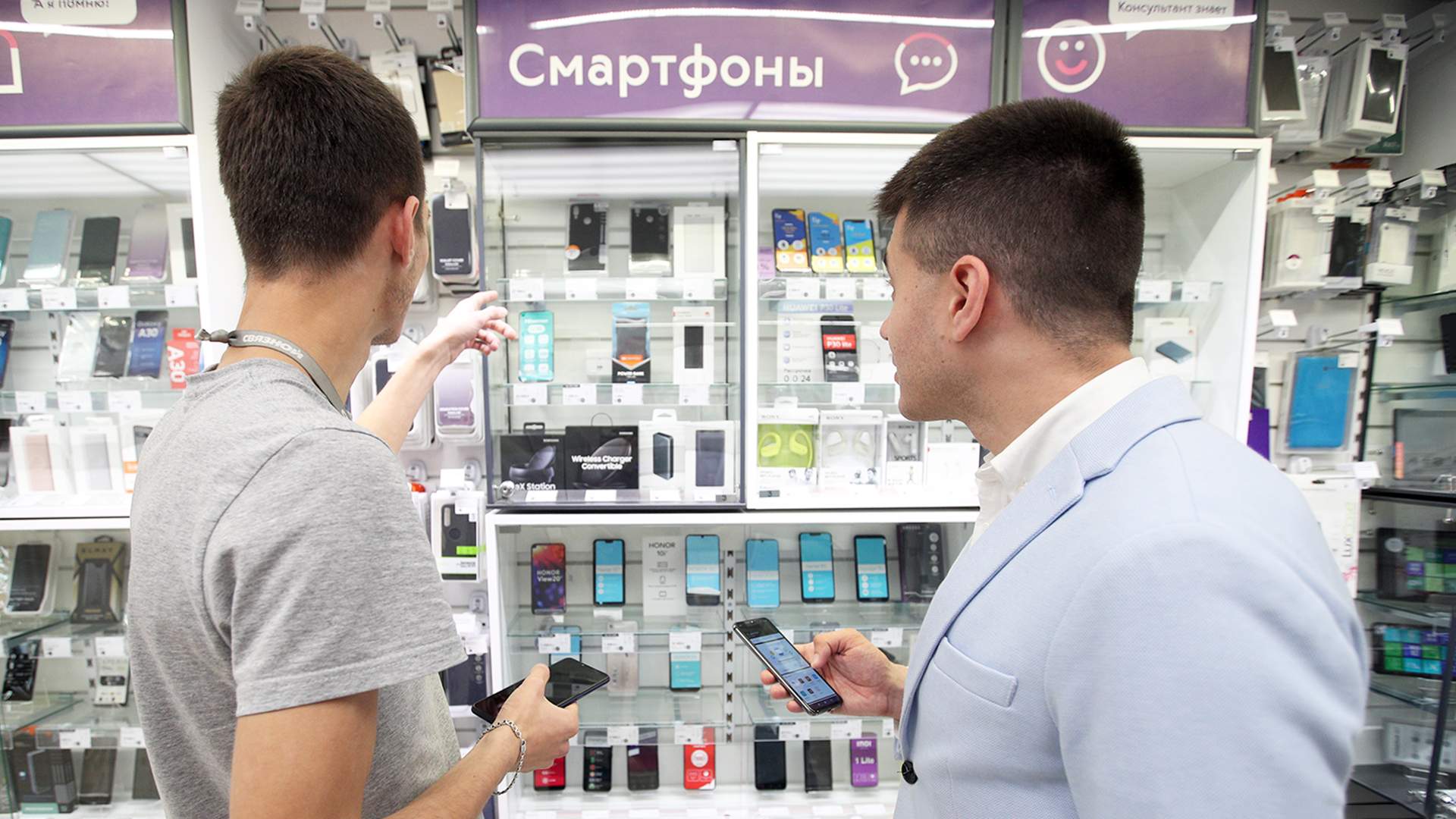 Продажа смартфонов в россии. Человек выбирает смартфон. Человек покупает смартфон. Человек со смартфоном в магазине. Магазин смартфонов.