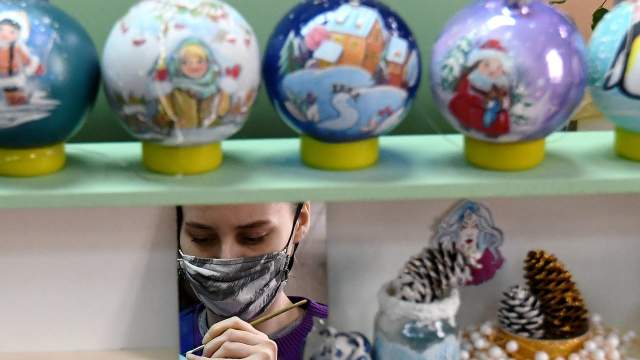 Художница отражается в зеркале, в то время как она расписывает стеклянный новогодний шар