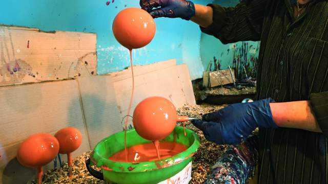 Художница опускает стеклянные шары в ведро с краской 