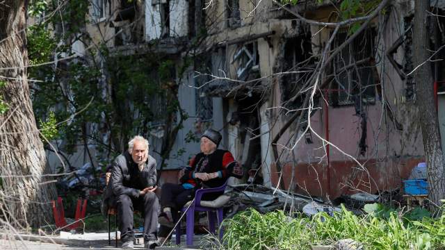 Local residents sit in a courtyard near a block of flats heavily damaged during Ukraine-Russia conflict in the southern port city of Mariupol