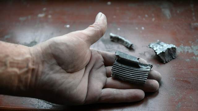 Мужчина держит в руках осколки снаряда, выпущенного ВСУ по Куйбышевскому району Донецка
