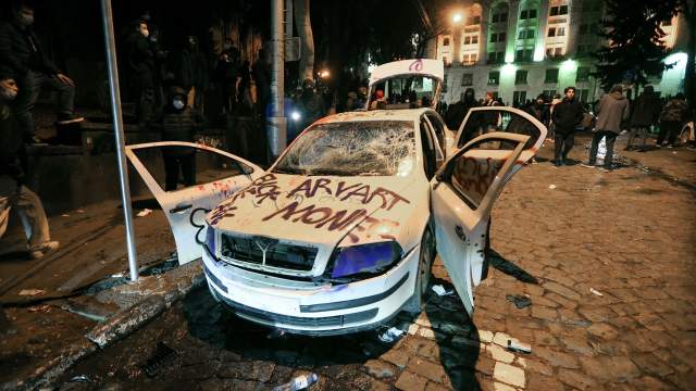 People stand near a car damaged during a protest against a draft law on "foreign agents", which critics say represents an authoritarian shift and could hurt Georgia's bid to join the European Union, in Tbilisi, Georgia, March 9