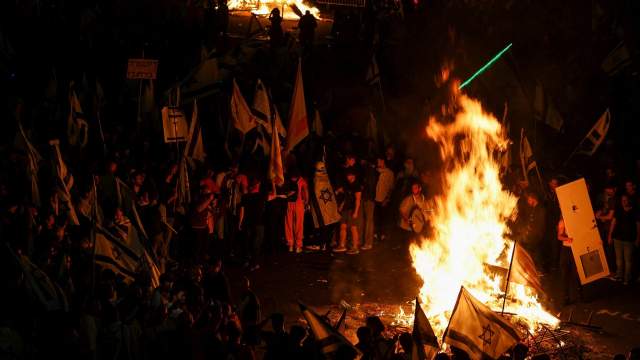 Fire burns as people attend a demonstration after Israeli Prime Minister Benjamin Netanyahu dismissed the defense minister and his nationalist coalition government presses on with its judicial overhaul, in Tel Aviv
