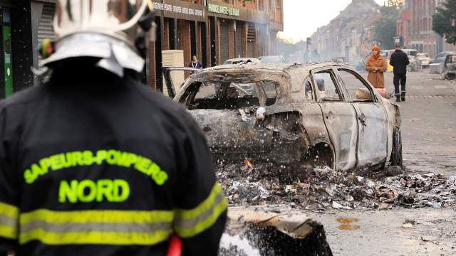 Nanterre'de Roubaix'in Alma semtinde bir trafik durması sırasında bir Fransız polis memuru tarafından öldürülen 17 yaşındaki Nahel adlı bir gencin ölümünün ardından, protestocularla polis arasında gece çıkan çatışmalarda yanan bir arabadan çıkan yangını bir itfaiyeci söndürdü. kuzey Fransa, 30 Haziran 2023.