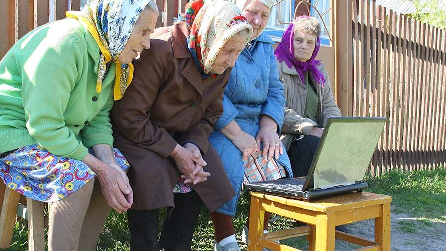 Пенсионерки смотрят телепередачу на ноутбуке во дворе сельского дома в Ивановской области