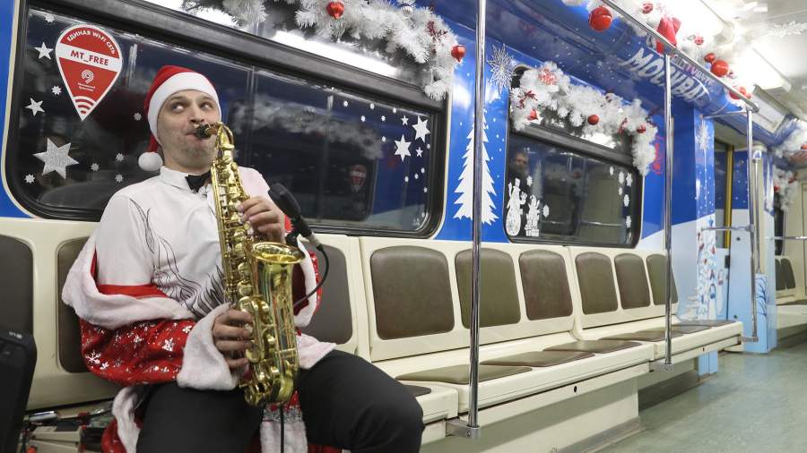 Мужчина играет на саксофоне в пустом вагоне метро, украшенном к Новому году