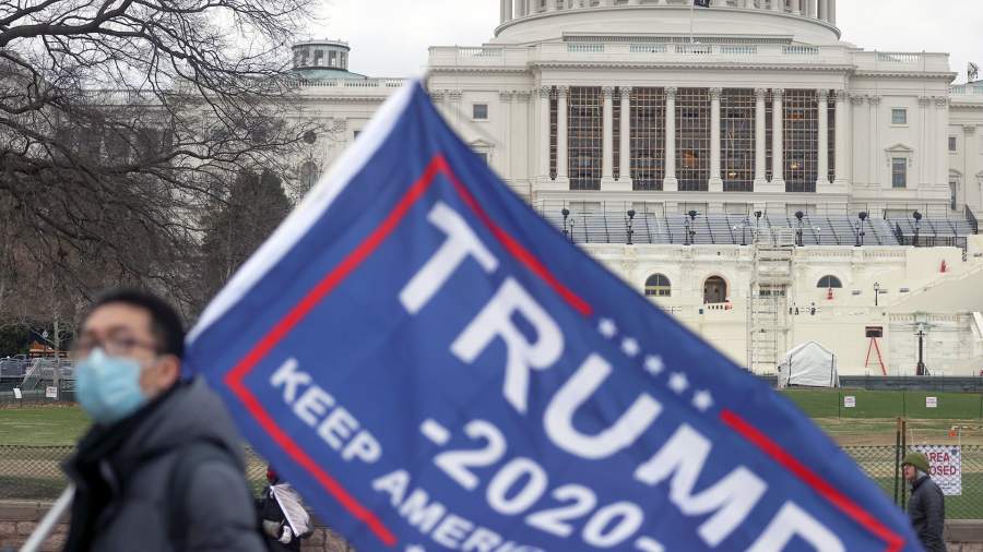 У основания Капитолия возводится трибуна, в то время как сторонник Трампа держит флаг за несколько часов до заседания Конгресса для подтверждения голосования коллегии выборщиков за избранного президента Джо Байдена в Вашингтоне
