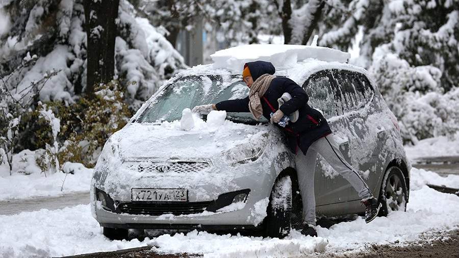 Женщина очищает свой автомобиль от снега 