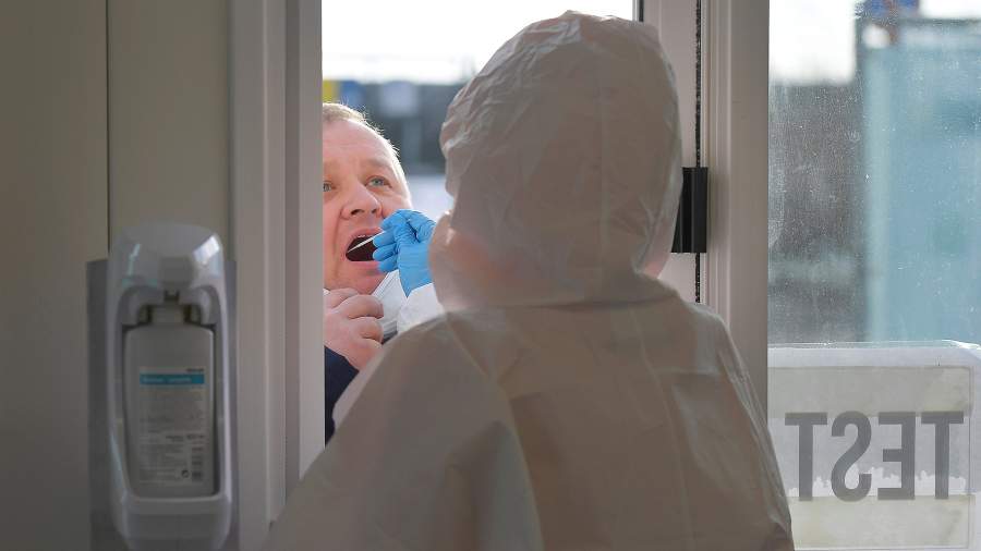 Медицинский работник берет мазок у водителя автомобиля в центре быстрого тестирования на фоне пандемии коронавируса (COVID-19) в Кодерсдорфе