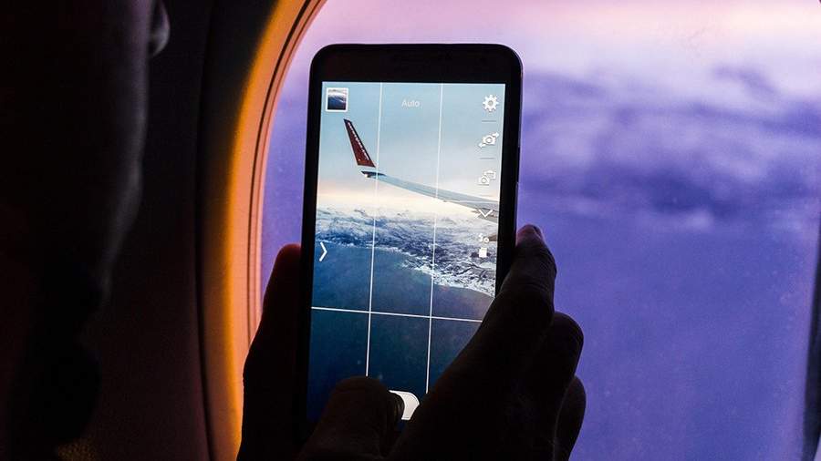 Мужчина снимает на смартфон вид из иллюминатора самолета