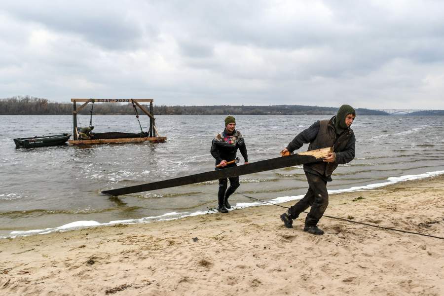 Люди по берегу тащат доску.