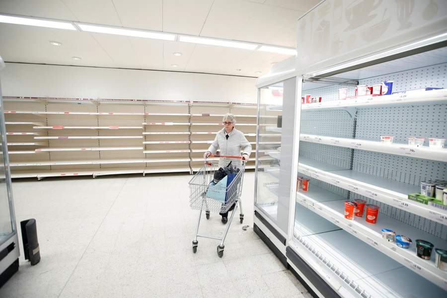 Покупательница толкает тележку рядом с пустыми полками в магазине