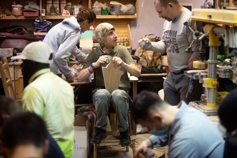 Подмастерья обрабатывают деревянные заготовки наждачной бумагой 