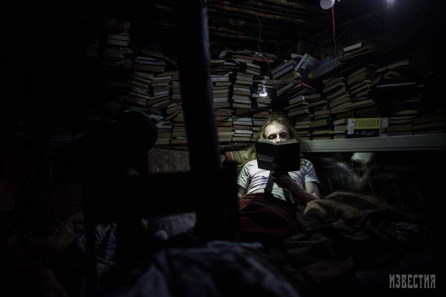 Юрий читает книгу перед с ном, у него в землянке небольшая библиотека 