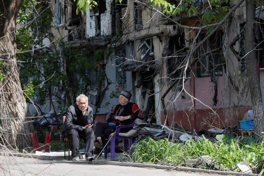 Local residents sit in a courtyard near a block of flats heavily damaged during Ukraine-Russia conflict in the southern port city of Mariupol