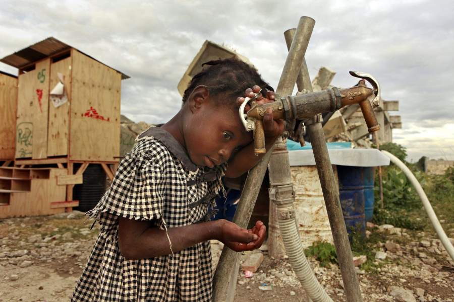 Девочка протягивает руки к сухому крану в лагере в Порто-Пренсе