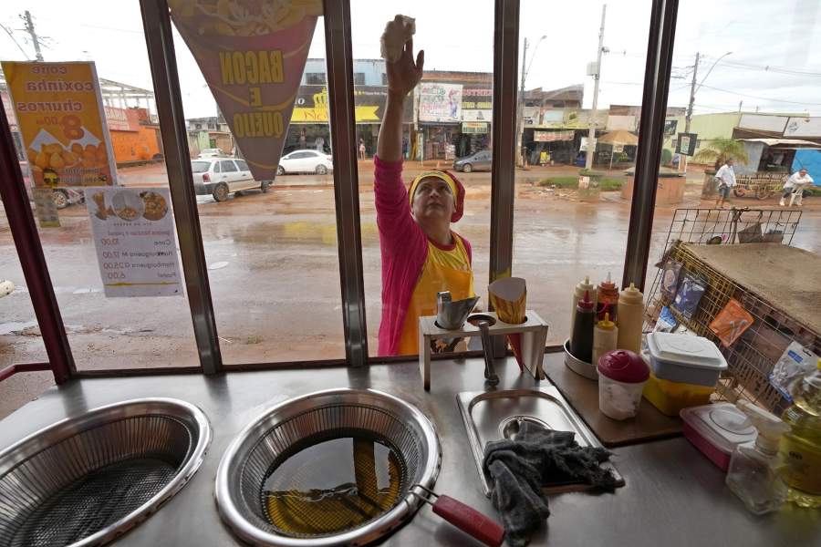 Francisca Celia cleans the glass of her cart where she sells chips, on the main street of the Sol Nascente favela of Brasilia, Brazil, Monday, March 20, 2023. Celia said residents still need basic sanitation and infrastructure but that available plots of land are much bigger than in other favelas in Rio and that it isn’t nearly as disorganized or dangerous
