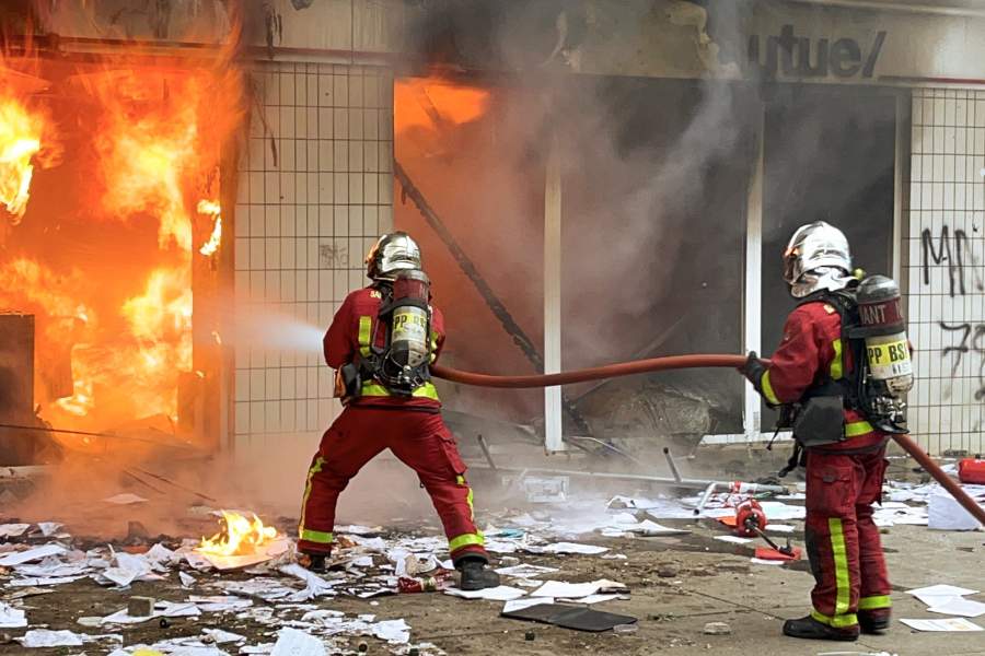 Сотрудники пожарной службы тушат пожар в одном из зданий во время беспорядков во французском Нантере.