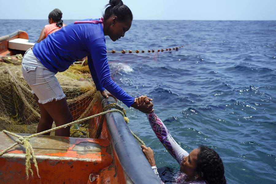 Рыбак Каролина Чавес забирается в лодку с помощью коллеги у побережья Тухи, Венесуэла, пятница, 9 июня 2023 года. Чавес, начавшая рыбачить в 11 лет, два года назад чуть не потеряла левую руку, когда она запуталась с веревка, когда она и другие пытались поднять тяжелую сеть, и их лодки столкнулись, отрезав ей половину среднего пальца.