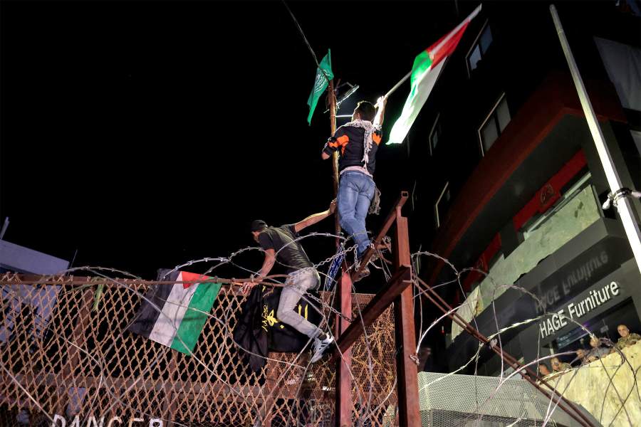 Ливанские протестующие в Бейруте машут палестинскими флагами, взбираясь на забор посольства США