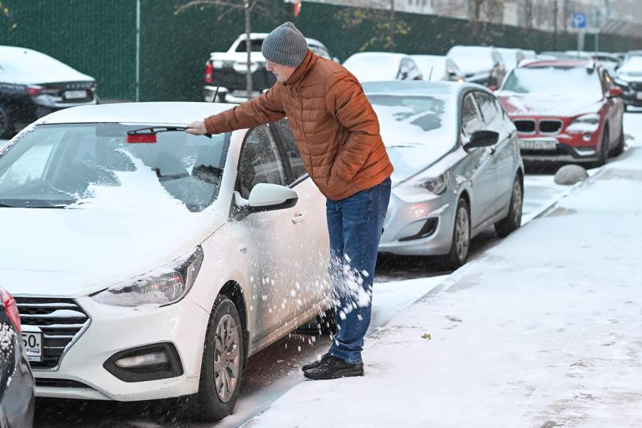 Мужчина расчищает автомобиль от снега в одном из дворов Москвы. В столичном регионе выпал первый снег. До конца дня 27 октября МЧС обещает метель, гололедицу и порывы ветра до 15 м/с.