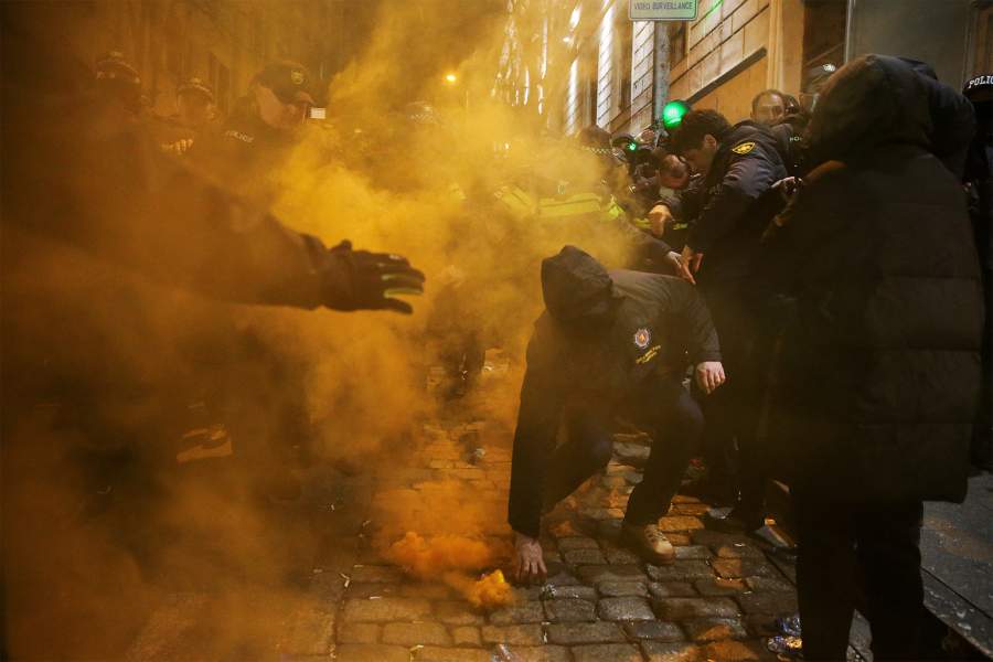 Полицейский идет за дымовой гранатой, когда сторонники грузинской оппозиции присутствуют на митинге протеста после того, как правительство приостановило процесс подачи заявок на вступление в ЕС до 2028 года, перед зданием парламента в Тбилиси, Грузия, 29 ноября 2024 года