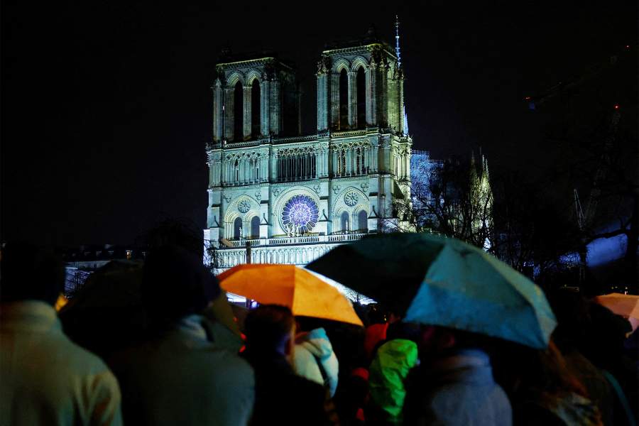 Люди защищаются от дождя под зонтиками, наблюдая на экране за церемонией открытия богослужения собора Парижской Богоматери, спустя пять с половиной лет после того, как пожар уничтожил готический шедевр, в рамках церемонии, посвященной открытию собора. открытие после реставрации, Париж, Франция, 7 декабря 2024 года
