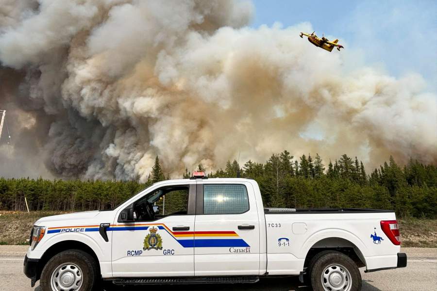 Патрульный автомобиль Королевской канадской конной полиции (RCMP) припаркован, в то время как водометный бомбардировщик пролетает над дымом от лесного пожара недалеко от Пас, Манитоба, Канада, 27 мая 2025 