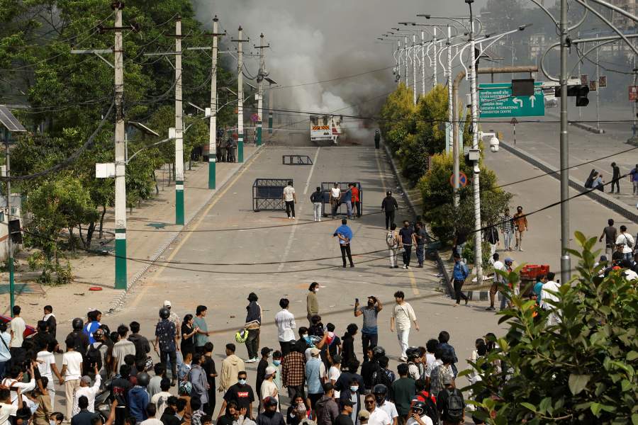 Клубы дыма поднимаются из машины скорой помощи рядом с сотрудниками спецподразделения полиции и демонстрантами во время акции протеста против коррупции и решения правительства заблокировать несколько социальных сетей в Катманду, Непал