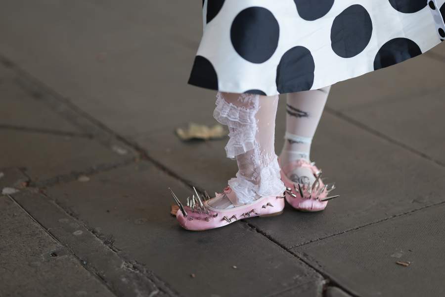 LONDON, ENGLAND - SEPTEMBER 19: A guest with black straight hair wearing a white and black polka-dot headscarf with ears, a white shirt with pink fur details, a white skirt with black polka dots, a black leather handbag, white socks, pink shoes with gold accents, colorful manicured nails, and silver jewelry outside Keburia Show during London Fashion Week on September 19, 2025 in London, England