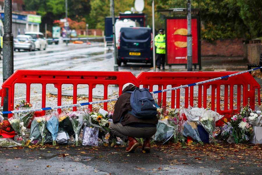 A person crouches next to floral tributes left near the Manchester synagogue, where multiple people were killed on Yom Kippur, in what police have declared a terrorist incident, in north Manchester, Britain, October 4, 2025. REUTERS/Hannah McKay