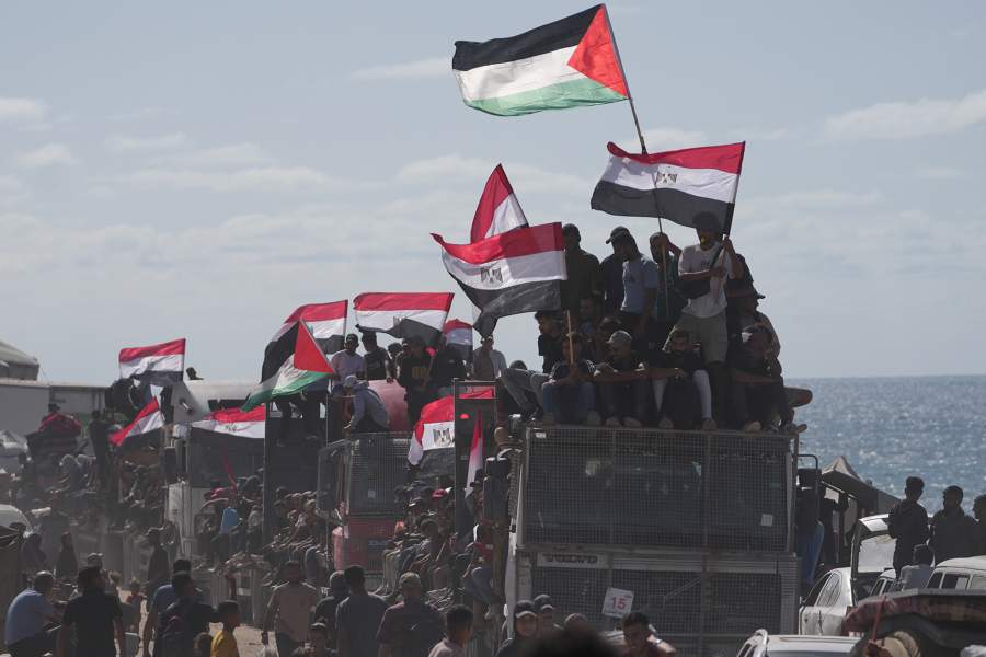 Displaced Palestinians ride on trucks loaded with belongings and wave Egyptian and Palestinian flags as they travel along the coastal road near Wadi Gaza in the central Gaza Strip, moving toward Gaza city, Saturday, Oct. 11, 2025, after Israel and Hamas agreed to a pause in their war and the release of the remaining hostages