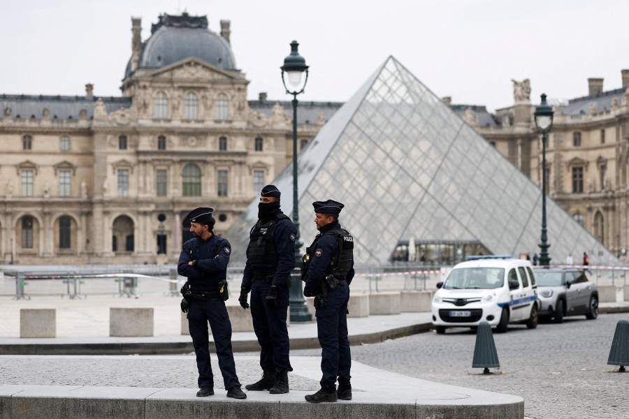 Police officers stand near the pyramid of the Louvre museum after reports of a robbery, in Paris, France, October 19, 2025