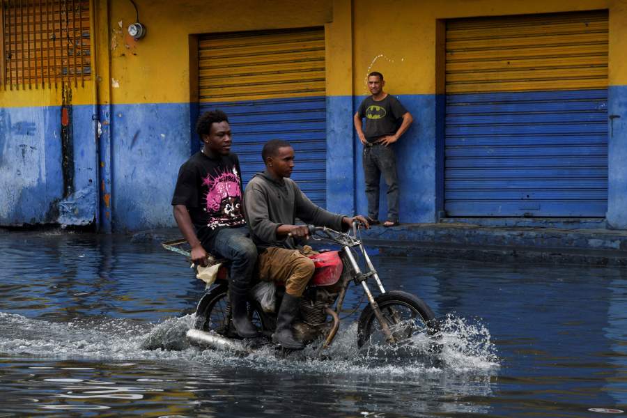 People transit on a motorcycle through a street flooded by rains caused by Tropical Storm Melissa, in Santo Domingo