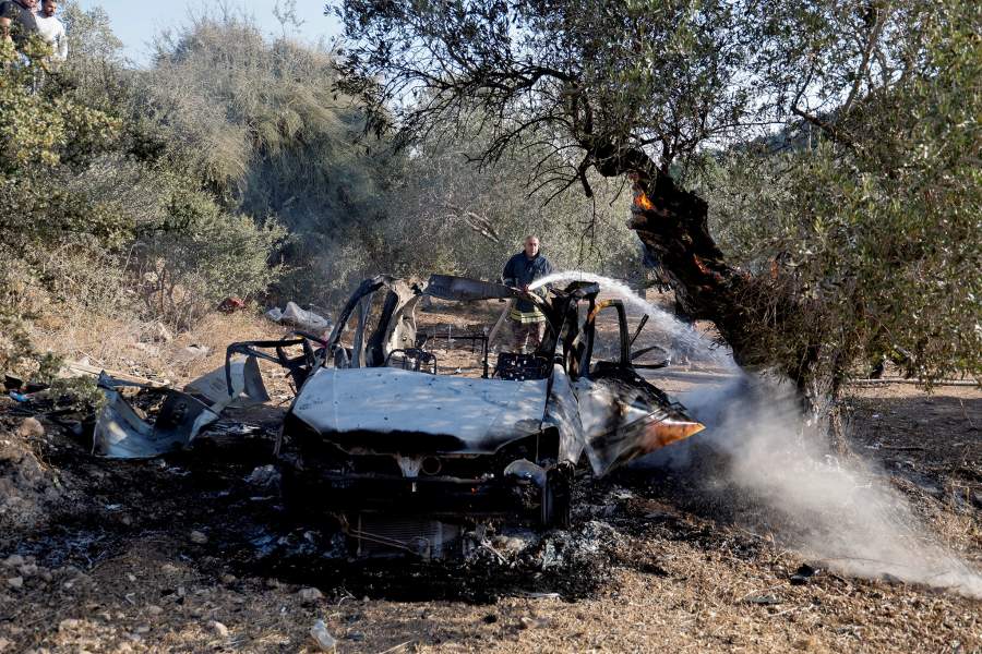A firefighter works to extinguish fire in a tree next to a burnt vehicle at the site where Israeli forces killed three Palestinians, near Jenin, in the Israeli occupied West Bank