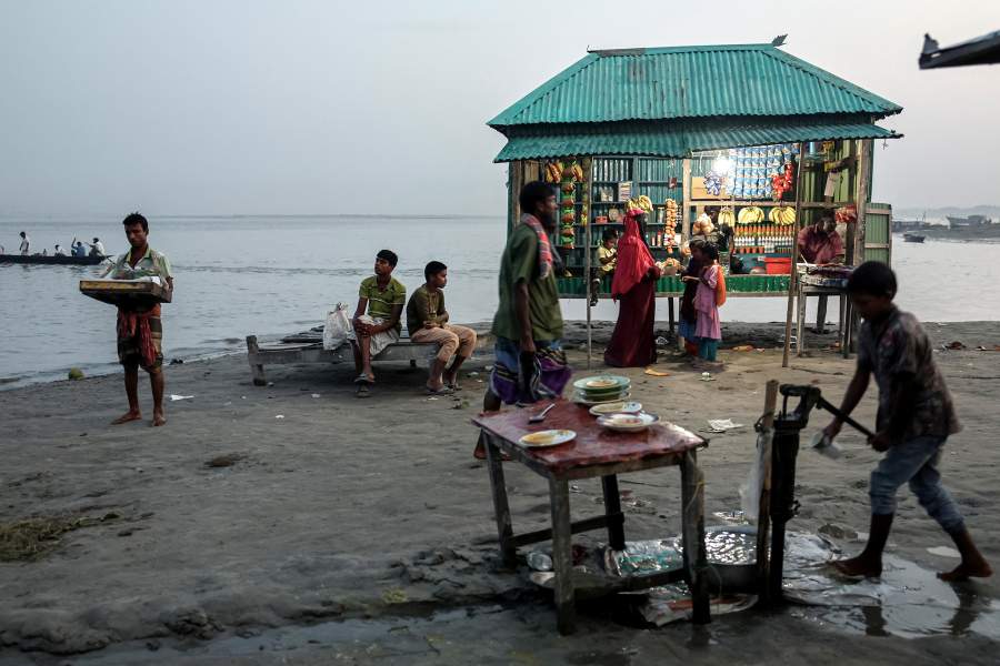 People sit near a shop on the bank of the Brahmaputra River in the evening, in Kurigram, Bangladesh, October 28, 2025. REUTERS/Mohammad Ponir Hossain