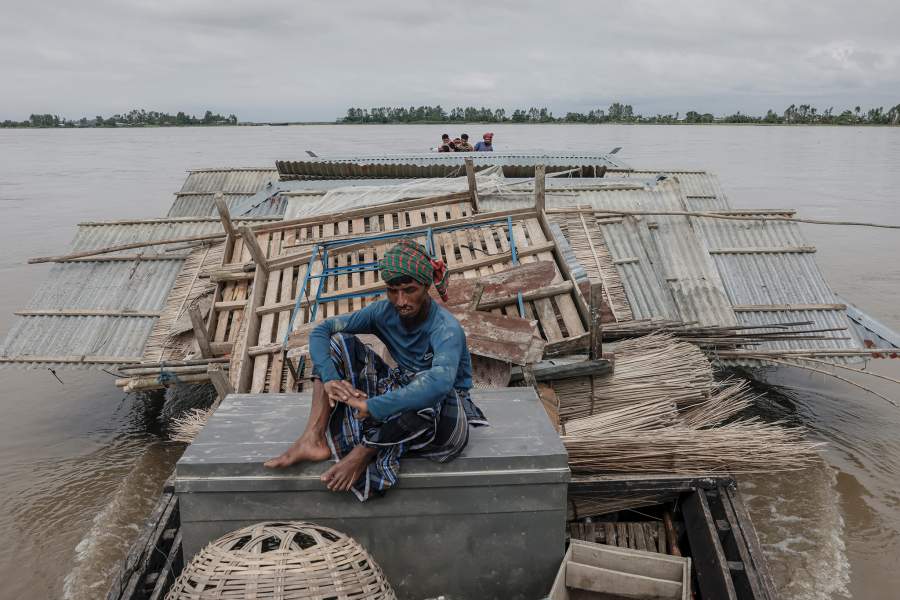 Hashem Ali, cousin of Kosim Uddin, 50, sits on a box as a boat carries the house to another island in the Brahmaputra River, with the current one on the verge of being destroyed by erosion, in Kurigram, Bangladesh, June 20, 2024. REUTERS/Mohammad Ponir Hossain