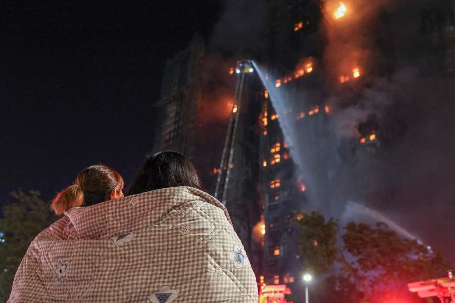 Residents wrapped in blankets watch flames engulf bamboo scaffolding at Wang Fuk Court housing estate after a major fire broke out, in Tai Po, Hong Kong