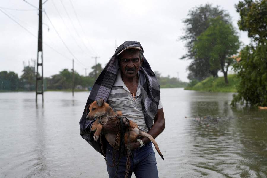 A man carrying a dog walks along a flooded street following heavy rainfall in Wellampitiya