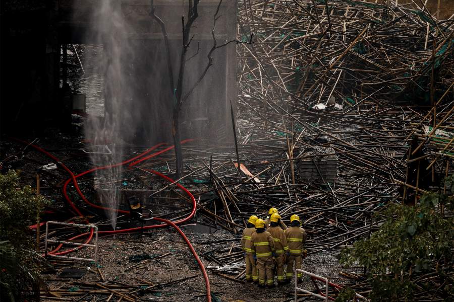 Firefighters gather next to bamboo scaffolding debris at the Wang Fuk Court housing complex after the deadly fire, in Tai Po, Hong Kong, China