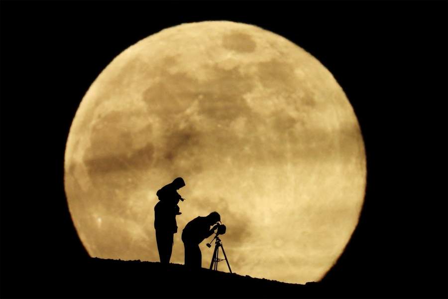 A couple and their daughter use a telescope to observe the last supermoon of 2025, known as the Cold Moon