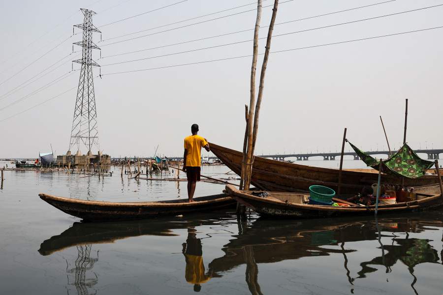 A person stands on a boat near a powerline as authorities burn remaining structures in their Makoko riverine community in Lagos, Nigeria, January 25, 2026. Officials are removing structures, including homes and schools, near power lines, in a wider push to recover lagoon side land from the historic fishing community often called the "Venice of Nigeria." REUTERS/Sodiq Adelakun