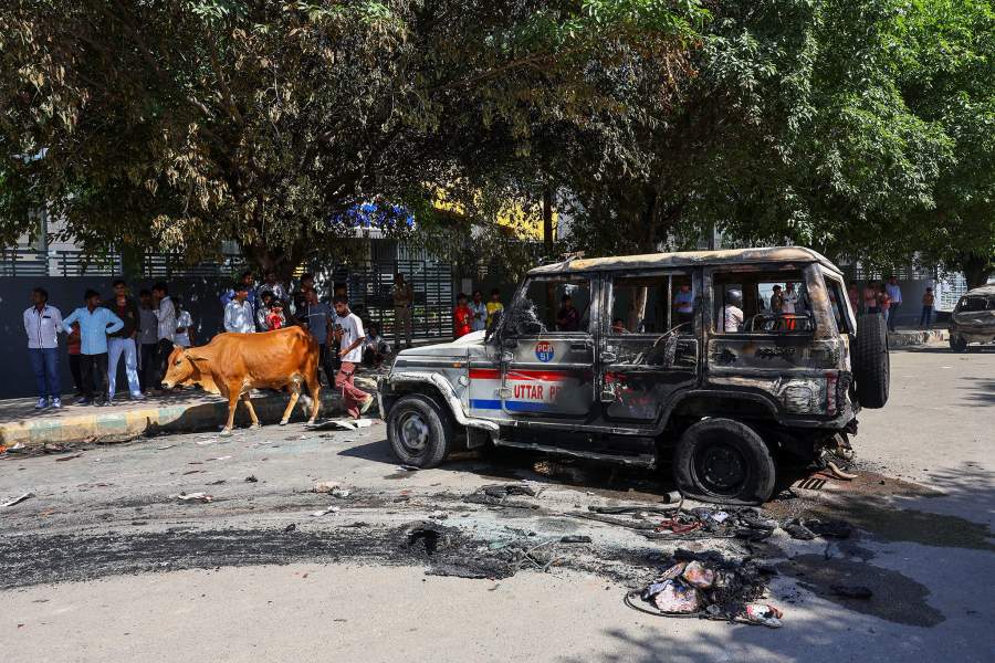 A cow walks past a burnt police vehicle during a workers' protest, after factory workers demanded a wage hike, amid soaring living costs due to disruptions caused by the U.S.-Israeli conflict with Iran, in Noida, India's industrial hub town in the state of Uttar Pradesh, India, April 13, 2026