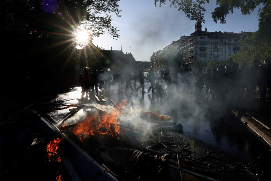 Riot police walk past fire as demonstrators hold banners during a protest against the upcoming G7 summit in Evian-les-Bains in France, in Geneva, Switzerland, June 14, 2026.