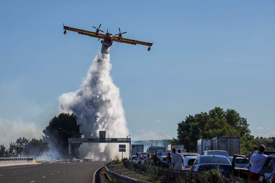 People watch as a firefighting plane flies to battle wildfire near the A9 motorway near Beziers, France, July 3, 2026